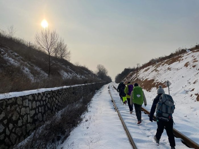 Four people walk along a snow covered railway track.
